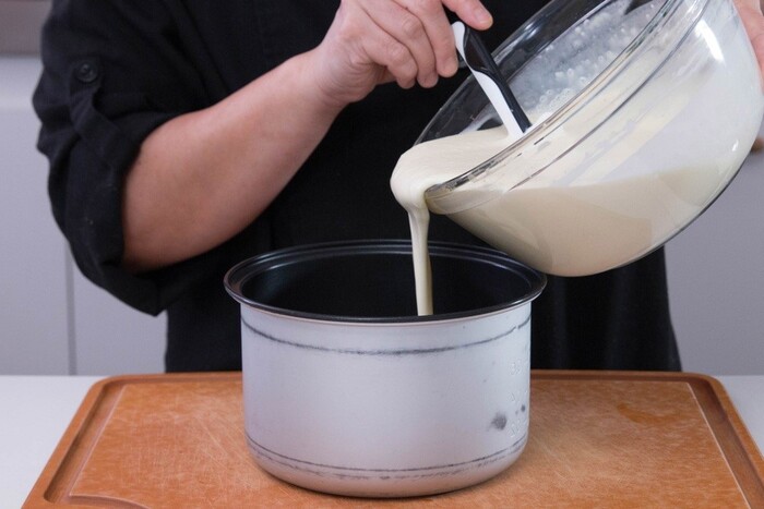 Chuẩn bị giấy nến hoặc bơ lót dưới đáy nồi, đổ bột bánh từ từ vào lòng nồi cơm điện